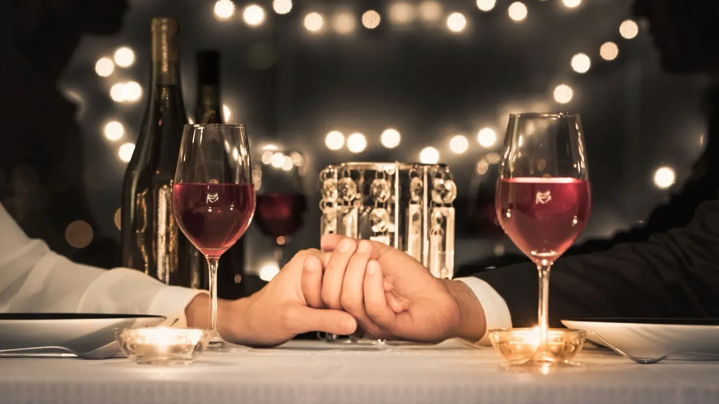 A couple holding hands across a candlelit dinner table with red wine